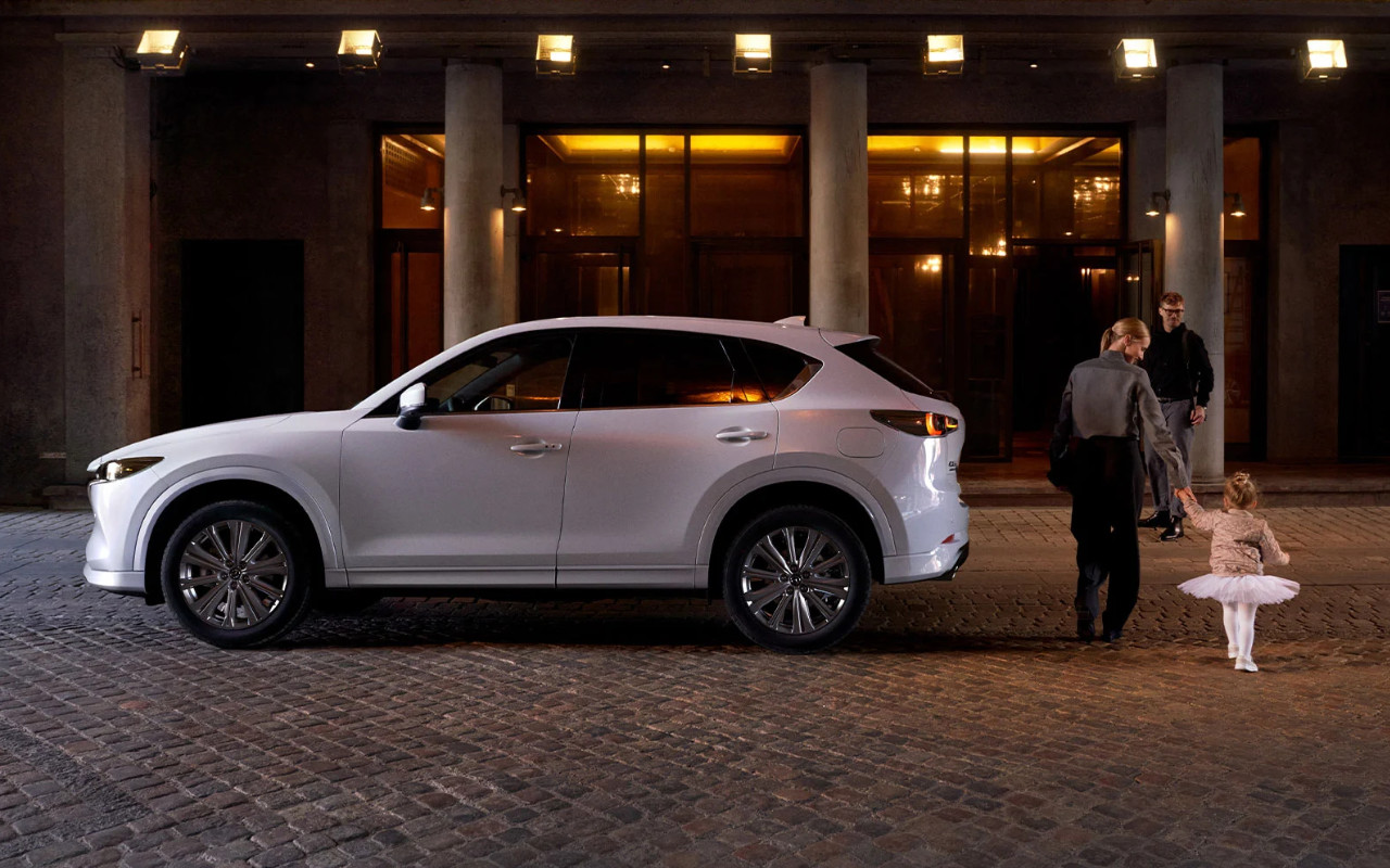 vue latérale d'une Mazda CX-5 2023 devant une théatre, à côté d'une mère et sa petite fille habillée en ballerine