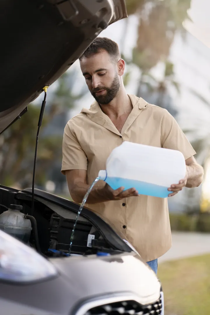 Homme faisant le plein de liquide lave-glace de sa voiture comme entretien régulier.