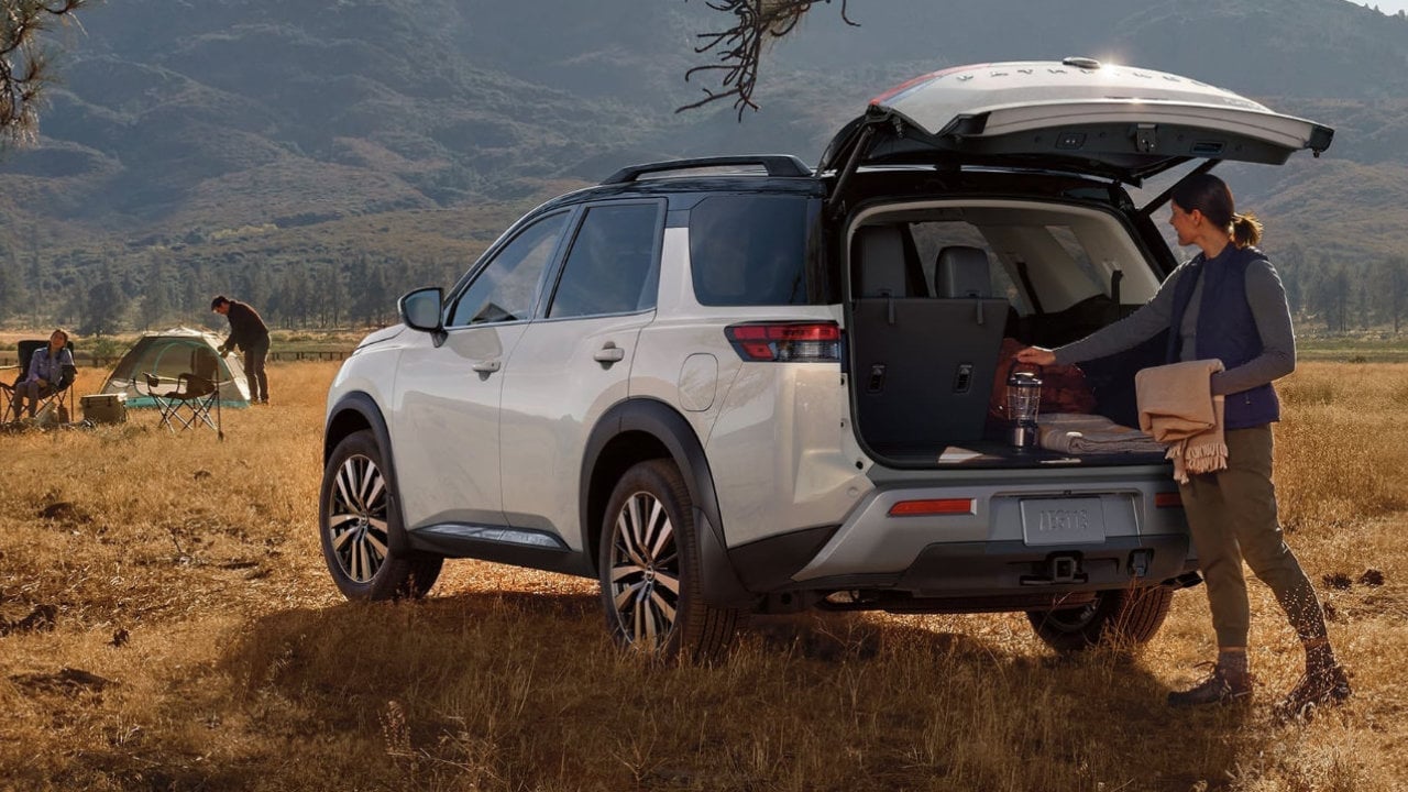 vue latérale arrière d'une Nissan Pathfinder 2023 et sa propriétaire en camping dans la nature